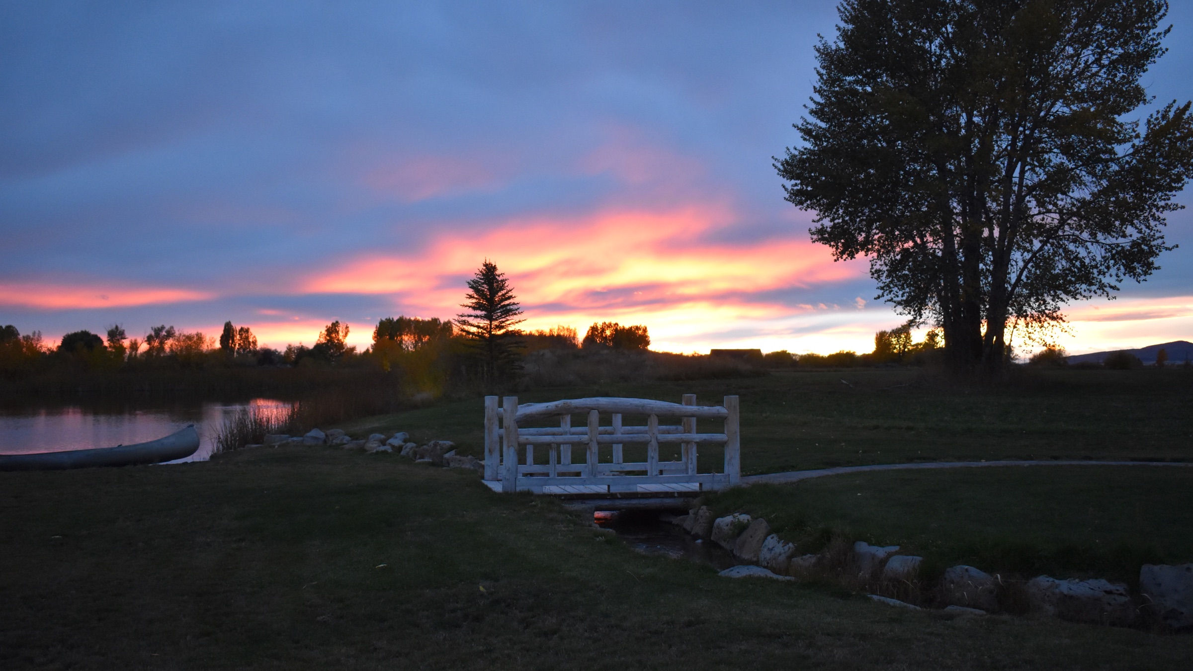 Sunset over the pond, log bridge, and canoe at Three Peaks Lodge